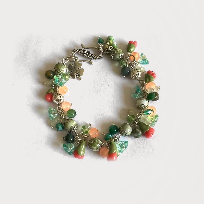 Pulsera Umbral de cristal verde, arcilla y pewter con pequeños dijes, sobre fondo claro